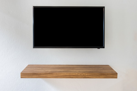 Black LED tv television screen on white wall background with modern wooden table in room.の写真素材