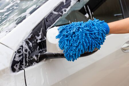 Woman hand with blue micro-fiber fabric washing side mirror modern car or cleaning automobile. Car wash conceptの写真素材