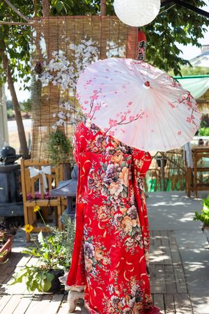 The girl is wearing a red traditional kimono, which is the national dress of Japan and Hold an umbrellaの写真素材
