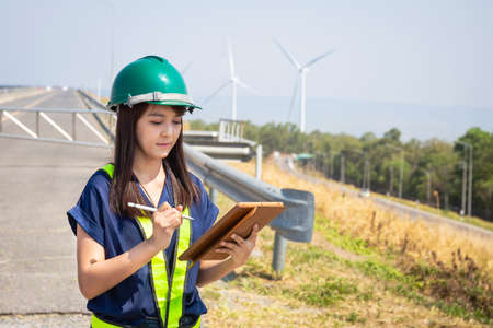 Asian woman engineers are checking and submitting reports outdoors on site power plant energy wind turbinesの写真素材