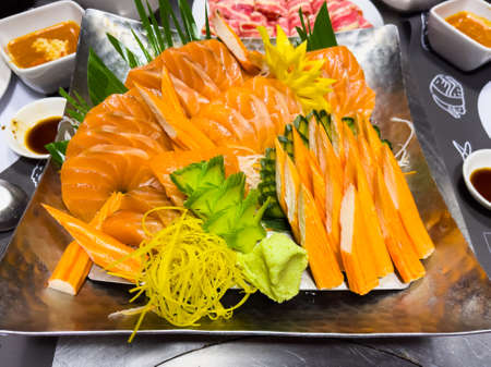 Salmon sashimi and crab sticks are placed in a plate on the dining table with vegetables and wasabi.の写真素材