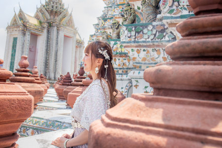 Young woman wearing traditional Thai dress stands at Wat Arun, a popular destination for tourists around the world. Bangkok Thailandの写真素材