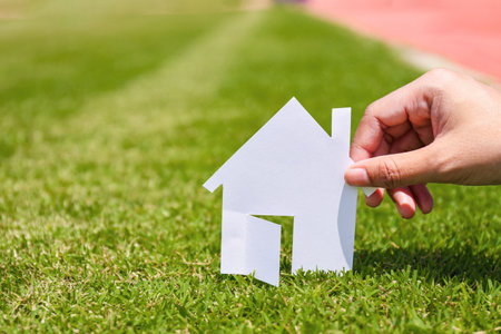 Hand hold home model from white paper on green grass background. Success dream life concept.の写真素材