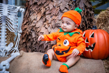 A little boy wearing a pumpkin costume and hat sits on a woven cloth to celebrate Halloween with a...