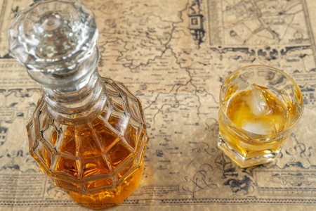 Whiskey or brandy decanter with a glass of whiskey on a table, covered in old parchment paper...