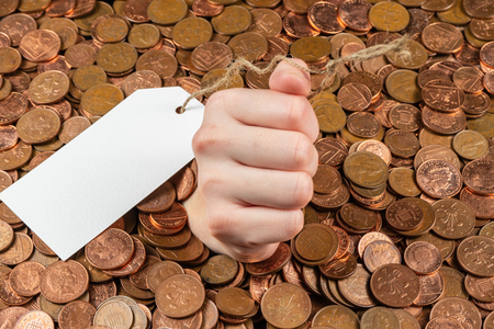The hand which is sticking out of heap of coins with sales tag.Copy space.