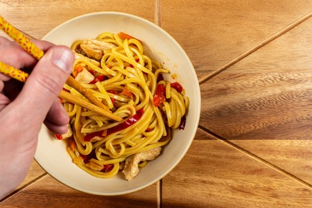Chicken chow mein and chopsticks on wooden table.の写真素材