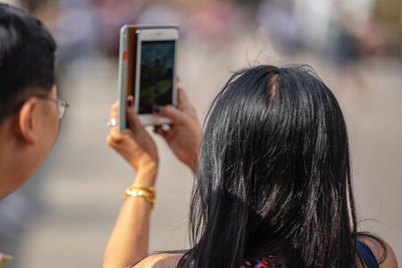 Rear view of Young woman takes photos using smart mobile cell phone cameraの写真素材