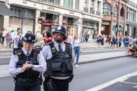 London, UK, July, 2019. Two British Police officers patrolling the streets of England wearing stab...