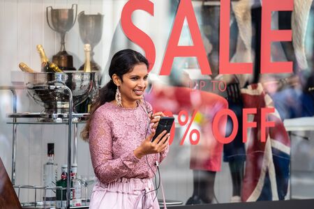 London, UK, July, 2019. Asian women in London, using mobile phone while shopping. Oxford Streetのeditorial素材