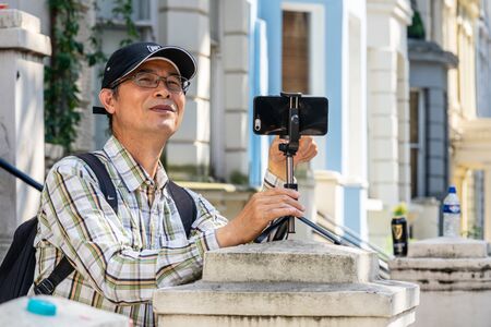 London, UK ,August 25, 2019. Elderly man filming video on his mobile phone using tripodのeditorial素材