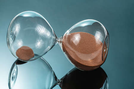 Hourglass with brown quartz sand lying on the mirror surfaceの写真素材