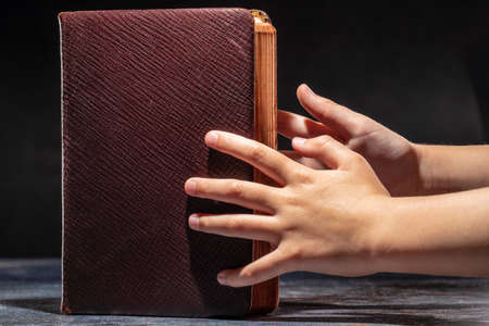 The childs hands stretching to the old book. The concept of thirst for knowledge
