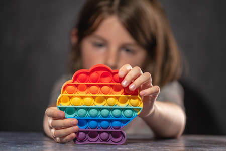 Little girl playing with rainbow colored pop silicone toy anti stressの写真素材