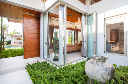 Interior and exterior design of pool villa which features living area, greenery garden, infinty swimming pool, wooden decking and sunbed surrounded by coconut treeの写真素材