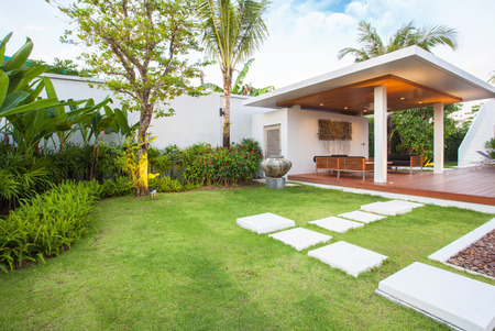 Interior and exterior design of pool villa which features living area, greenery garden, infinty swimming pool, wooden decking and sunbed surrounded by coconut treeの写真素材