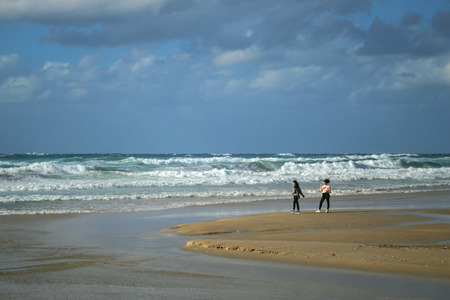 Netanya, Israel. November 21 2017: Young girl / teenager takes picture of her friend on seashore / seacoast of Sironit beach. Young active happy people. Lifestyle portrait of best friends.のeditorial素材