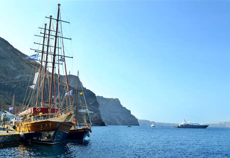 Sailboat / ship is at the pier of the island Santorini. On the background of the blue sea and dark caldera. Boats, yachts, ships in blue bay.の写真素材
