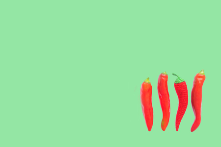 Set of three fresh raw hot red chili pepper and one crocheted pepper lie isolated on green...