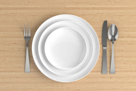 three empty plates, spoon, fork and knife on a wooden baseの写真素材