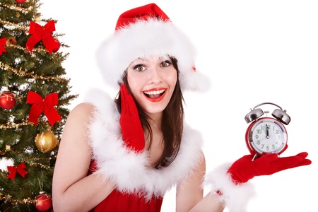 Girl in santa hat point on alarm clock by christmas tree.  Isolated.の写真素材