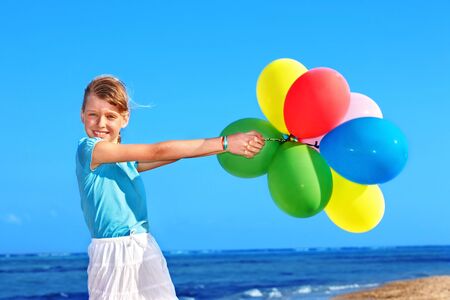 little girl playing with balloons at the beach.の写真素材