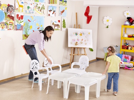 Child painting in preschool. Teacher help by little girl.の写真素材