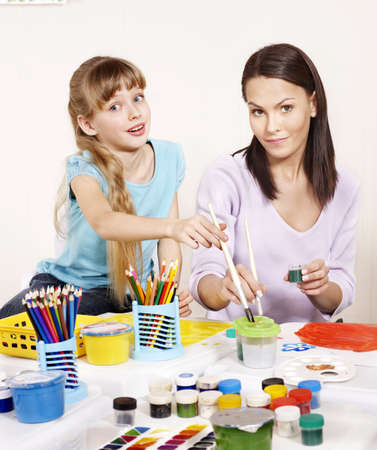 Child painting in preschool. Teacher help by little girl.の写真素材