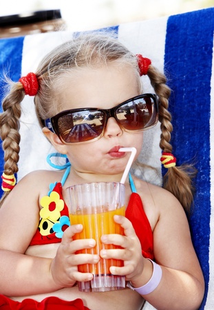 Little girl in glasses and red bikini drink orange juice.の写真素材