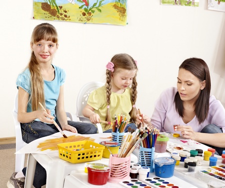 Child painting in preschool. Teacher help by little girl.の写真素材