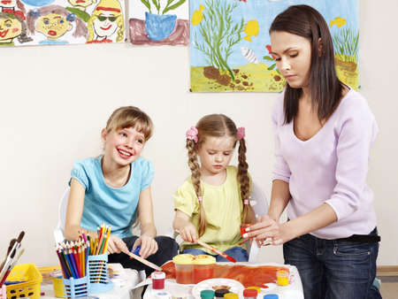Children painting in preschool. Teacher help by little girl.の写真素材