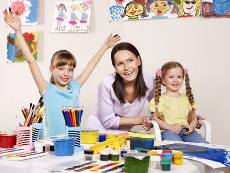 Children painting in preschool. Teacher help by little girl.の写真素材