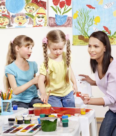 Children painting in preschool. Teacher help by little girl.の写真素材