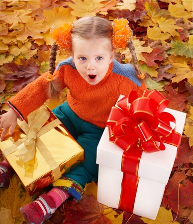 Little girl in autumn orange hat on leaves and gift box. Outdoor.の写真素材