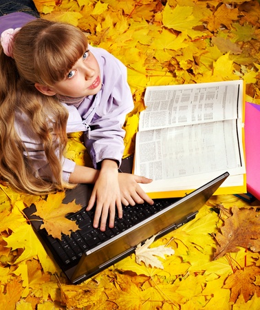 Childl in autumn leaves with laptop and books. Outdoors.の写真素材