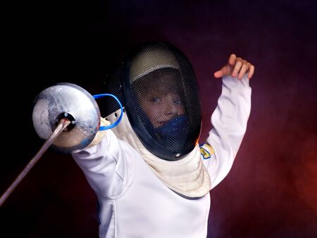 Child epee fencing lunge. Dark background.