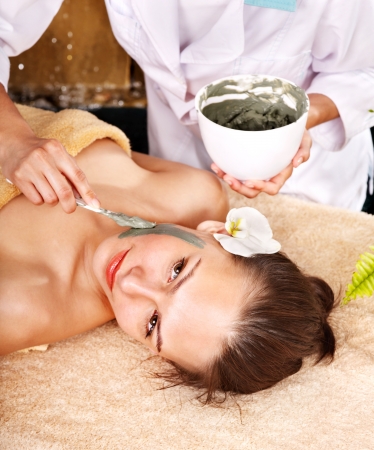 Beautiful girl having clay facial mask apply by beautician.の写真素材