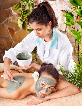 Beautiful girl having clay facial mask apply by beautician.の写真素材