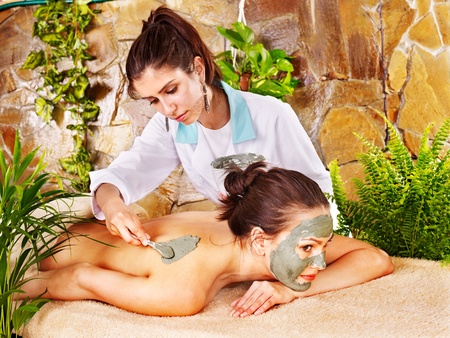 Beautiful girl having clay body mask apply by beautician.の写真素材