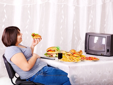 Overweight woman eating fast food and watching TV.の写真素材
