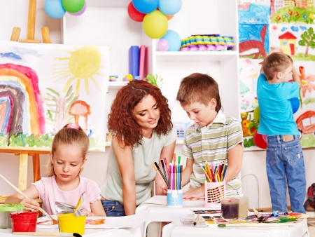 Children with teacher painting at easel in school.の写真素材