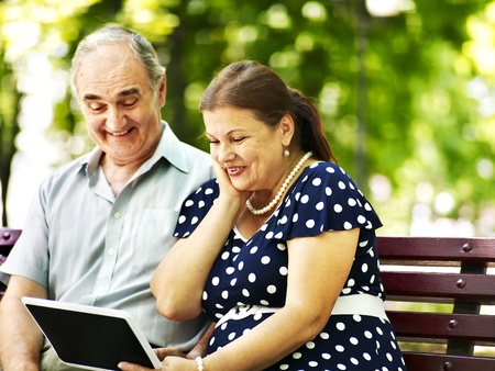 Old couple with tablet pc sit on bench  . Outdoor.