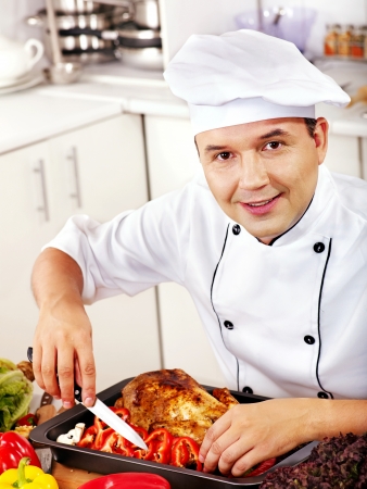 Happy man in chef hat cooking chicken.の写真素材