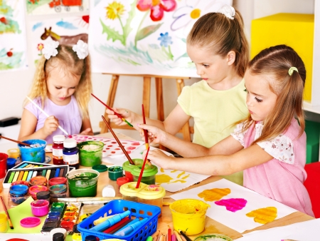 Child painting at easel in school. Teacher help.の写真素材