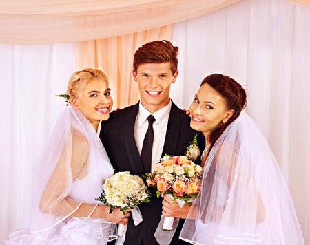 Happy wedding man and two bride holding flower bouquet.の写真素材