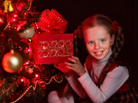Child with gift box near Christmas tree with glowing  lights.の写真素材