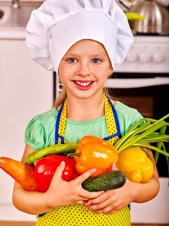 Child in cooking hat holding vegetable at kitchen.の写真素材