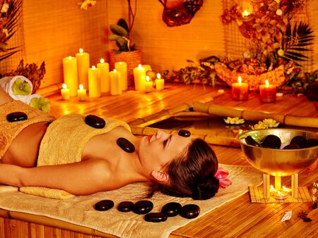 Woman getting stone therapy massage in bamboo spa. Stone therapy with burning candle.の写真素材