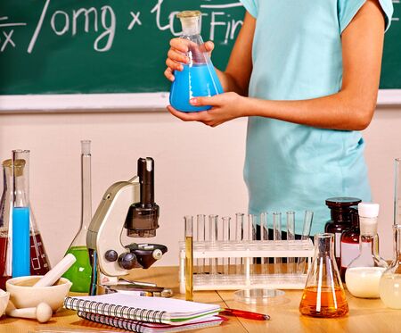 Kids hand holding flask in chemistry class with blackboard.の写真素材