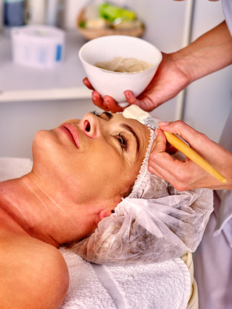 Woman middle-aged in hat take facial and neck clay mask in spa salon.の写真素材